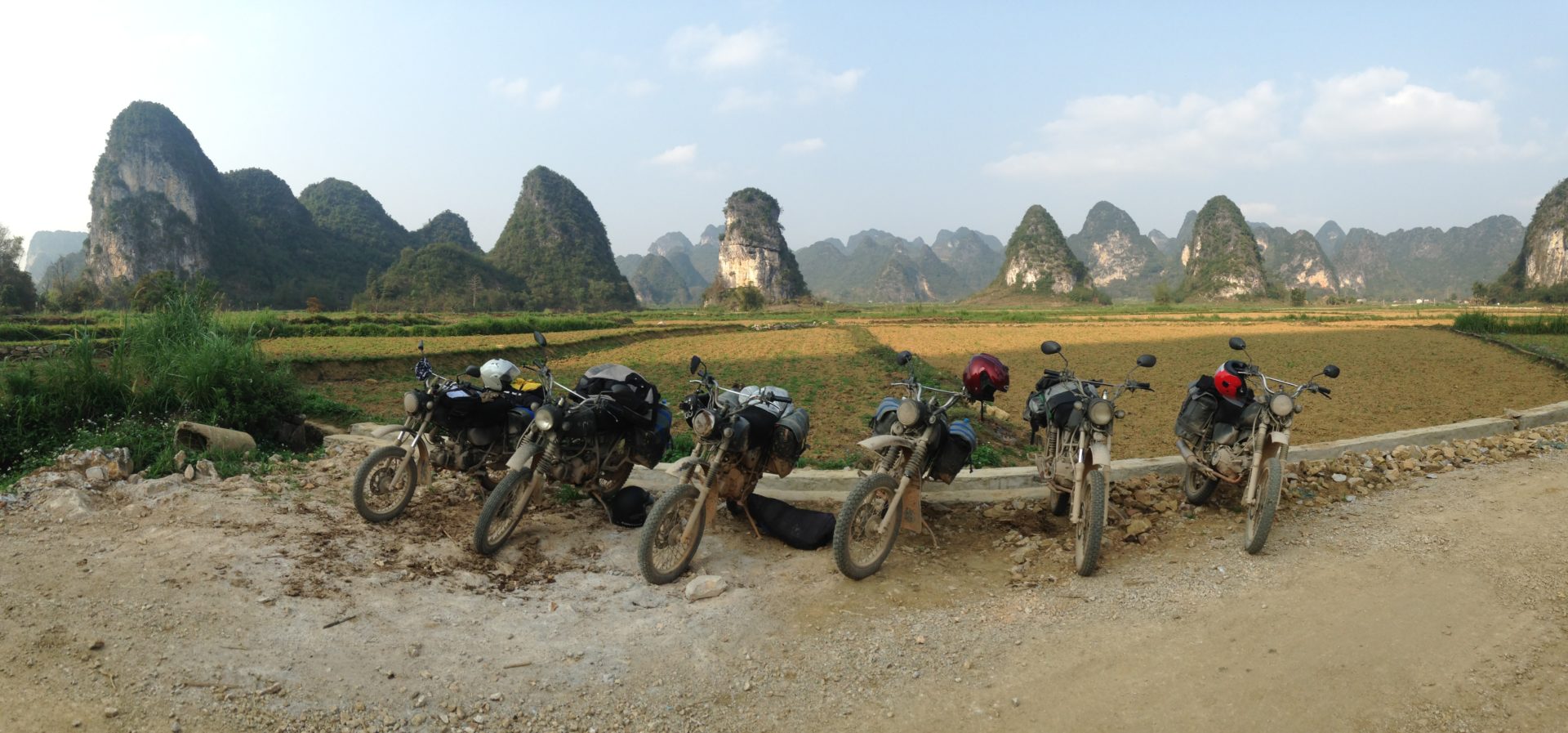 A fleet of Minsk motorbikes poised in a valley, with stunning karst mountains gracing the backdrop.