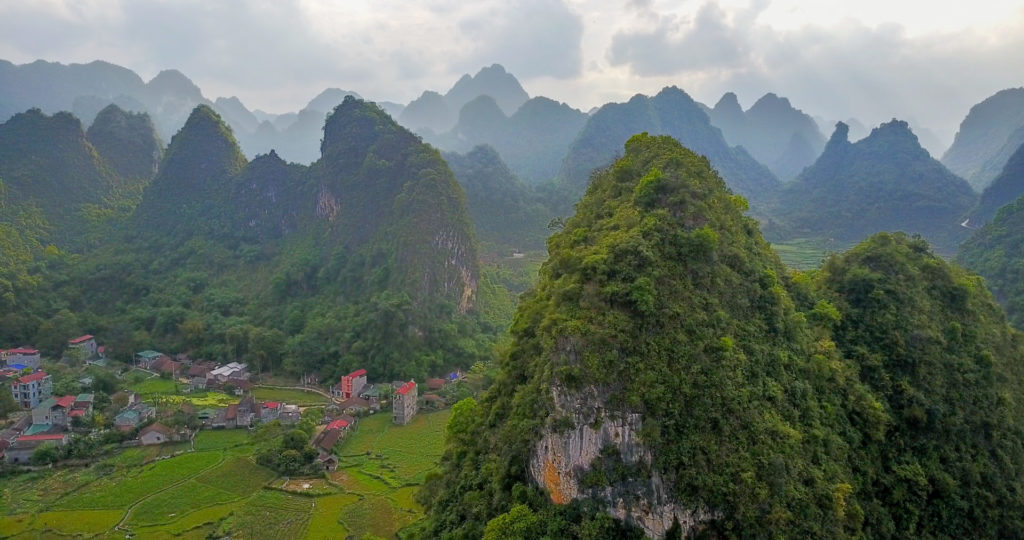 Scenic view of a village in Vietnam nestled at the base of towering karst limestone formations in a lush valley.