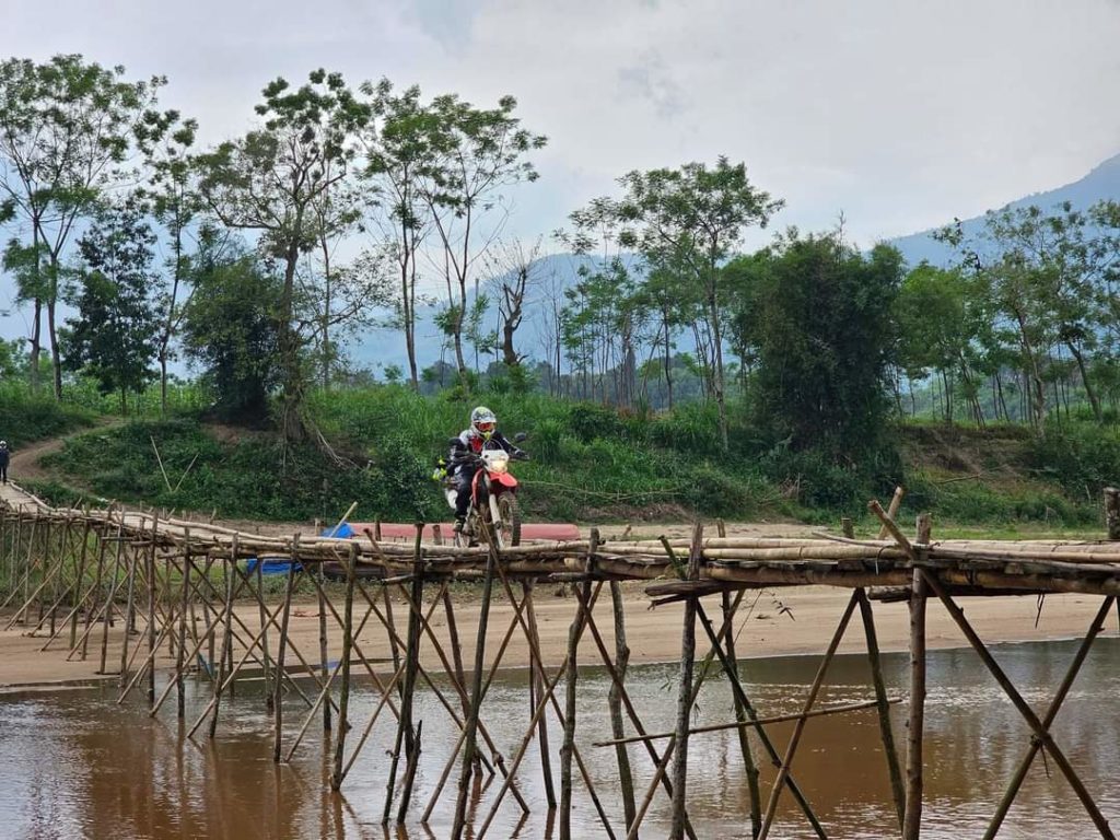 Motorbike rider crossing a traditional stick bridge over a river in a remote lowland area of Vietnam.