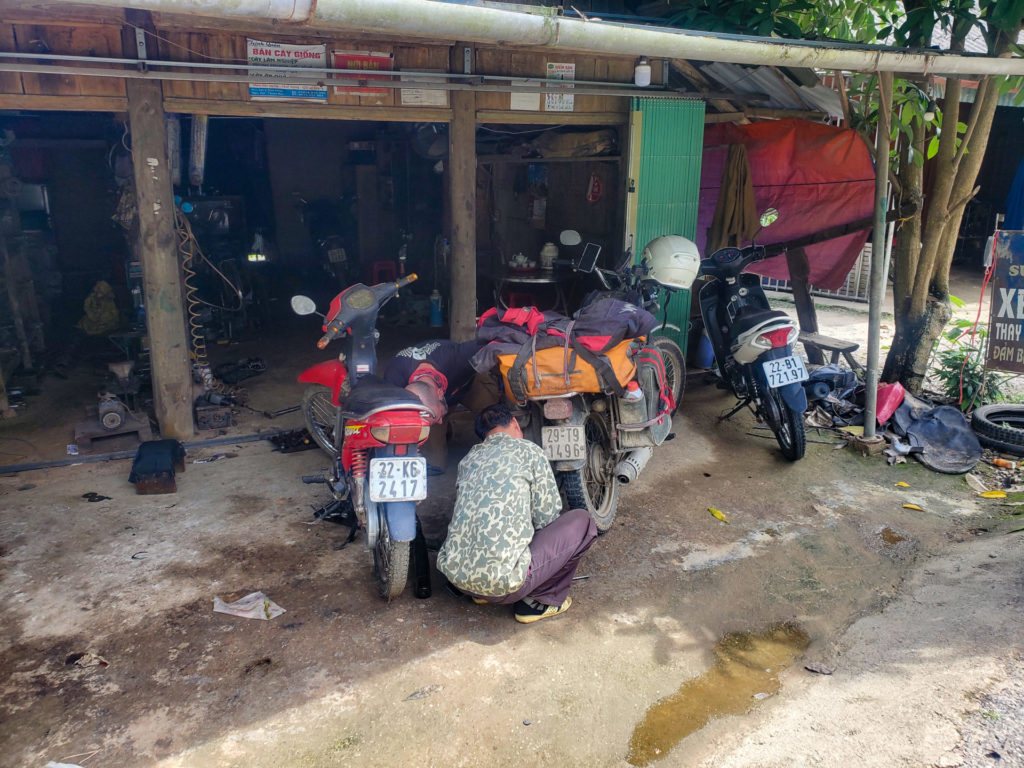 Field repair of a Minsk motorcycle during a Vietnam tour, showcasing the resilience and adaptability required on the road.