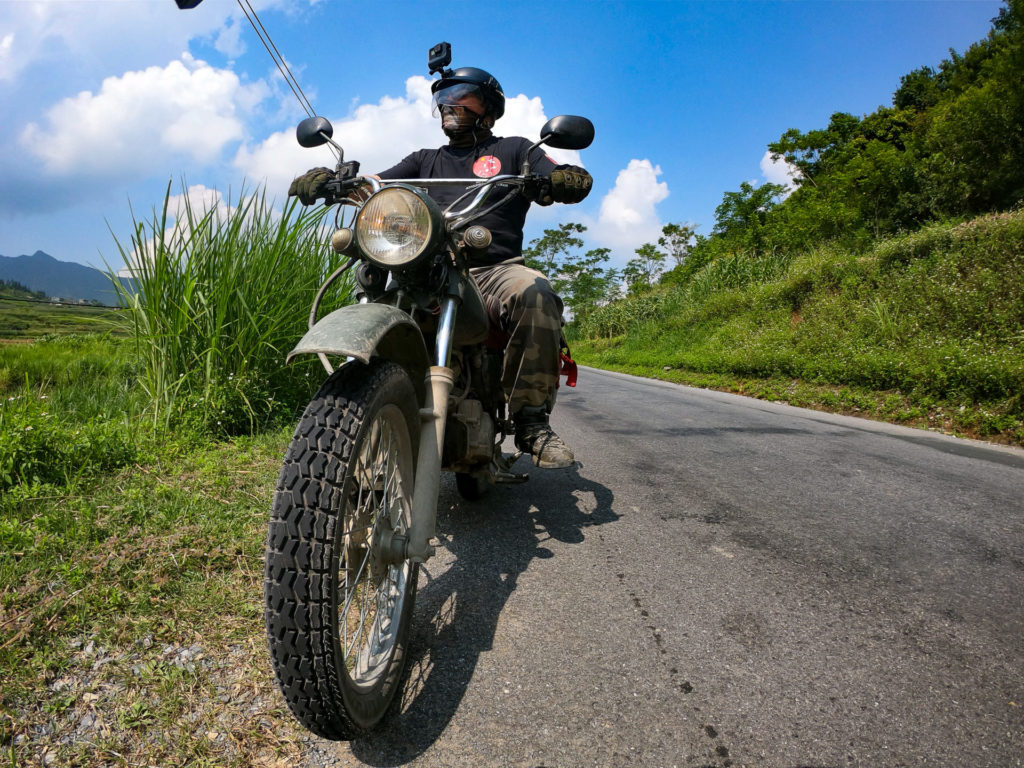 Rider on a Minsk motorcycle paused on a scenic route, surrounded by the lush greenery of Vietnam’s countryside.