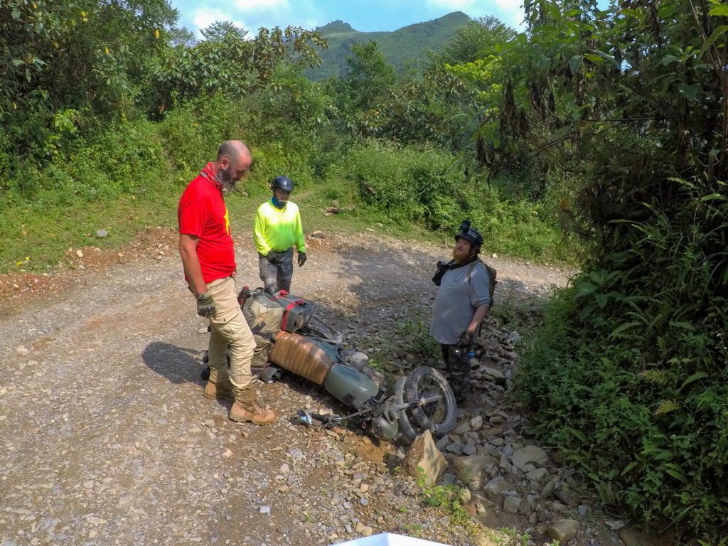 Adventurous riders assessing a fallen Minsk motorcycle on a rugged trail, embodying the unpredictability of Vietnam motorbike tours.